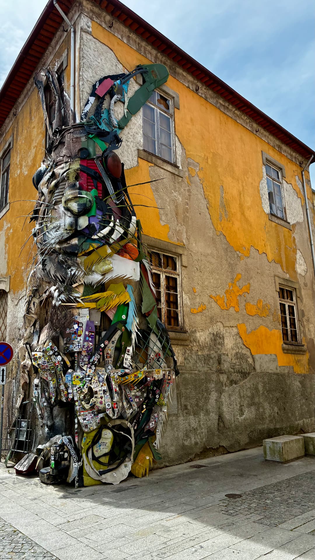Giant recycled-material rabbit street art on a yellow building in Porto