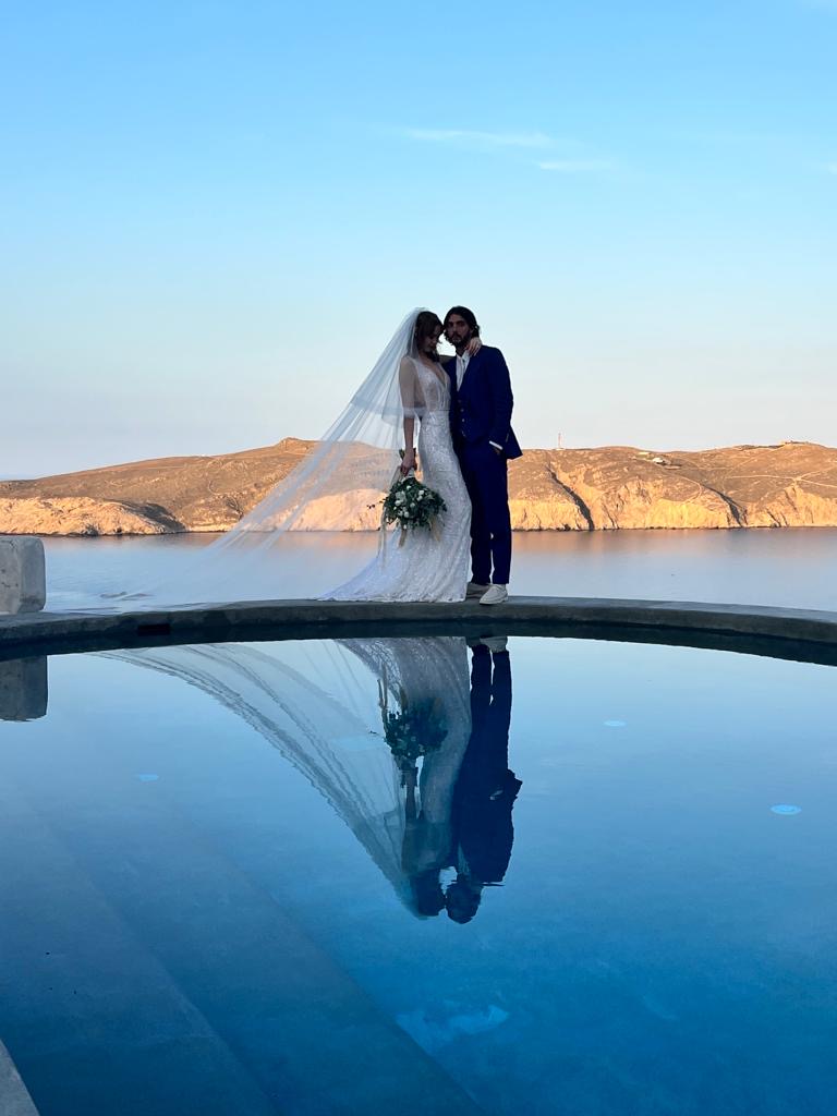Bride and groom reflected in an infinity pool overlooking the Greek islands